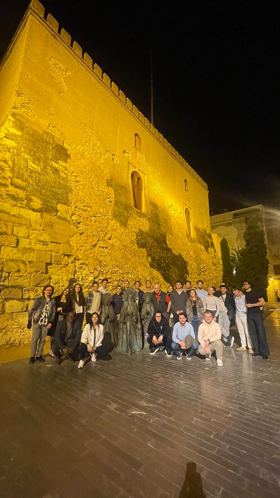 Group photo at night in front of a floodlit yellow wall in Alicante